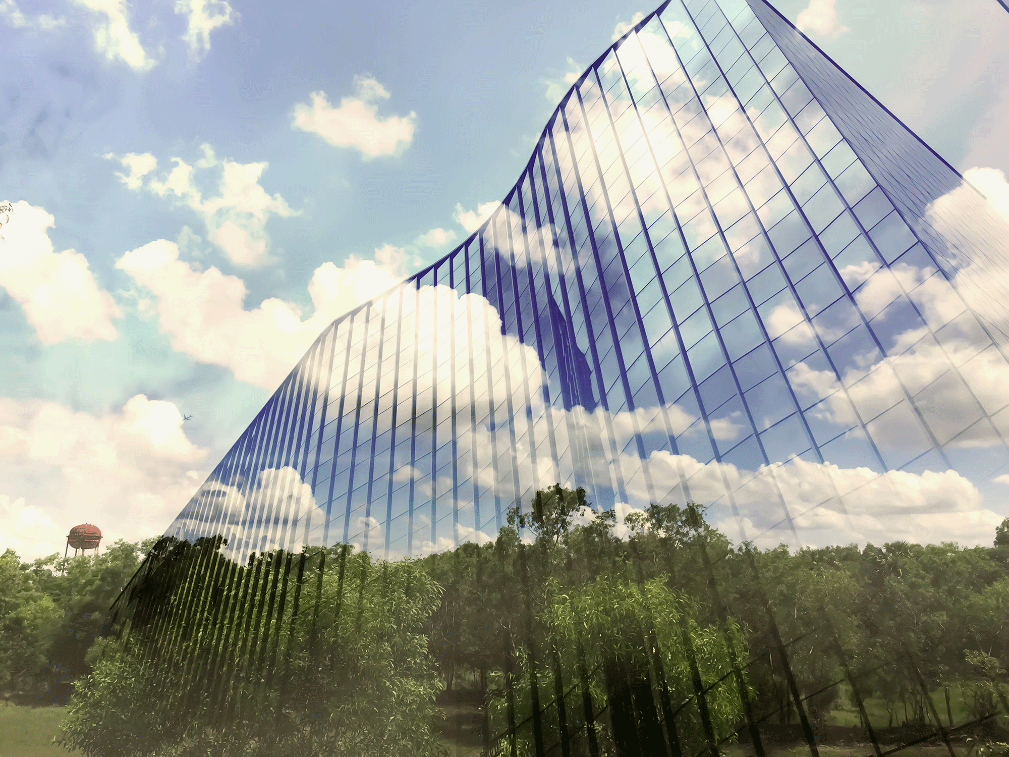 environmental sustainability - A glass building reflects a green forest and blue skies.