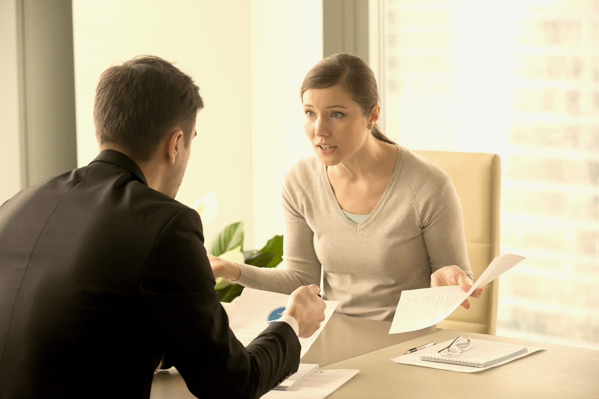 An angry business woman speaks with a colleague across a table of papers.