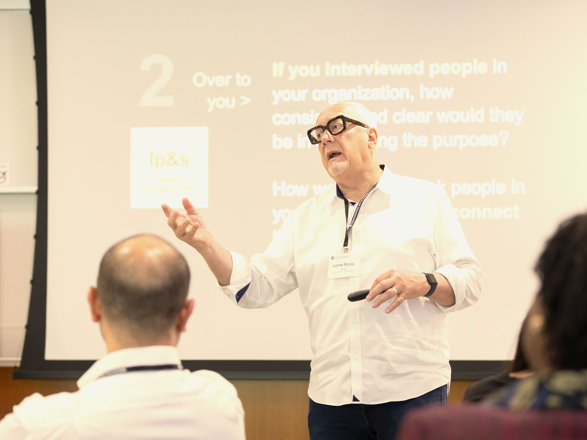 A professor with glasses and white hair speaking with his hands to a classroom of adult learners