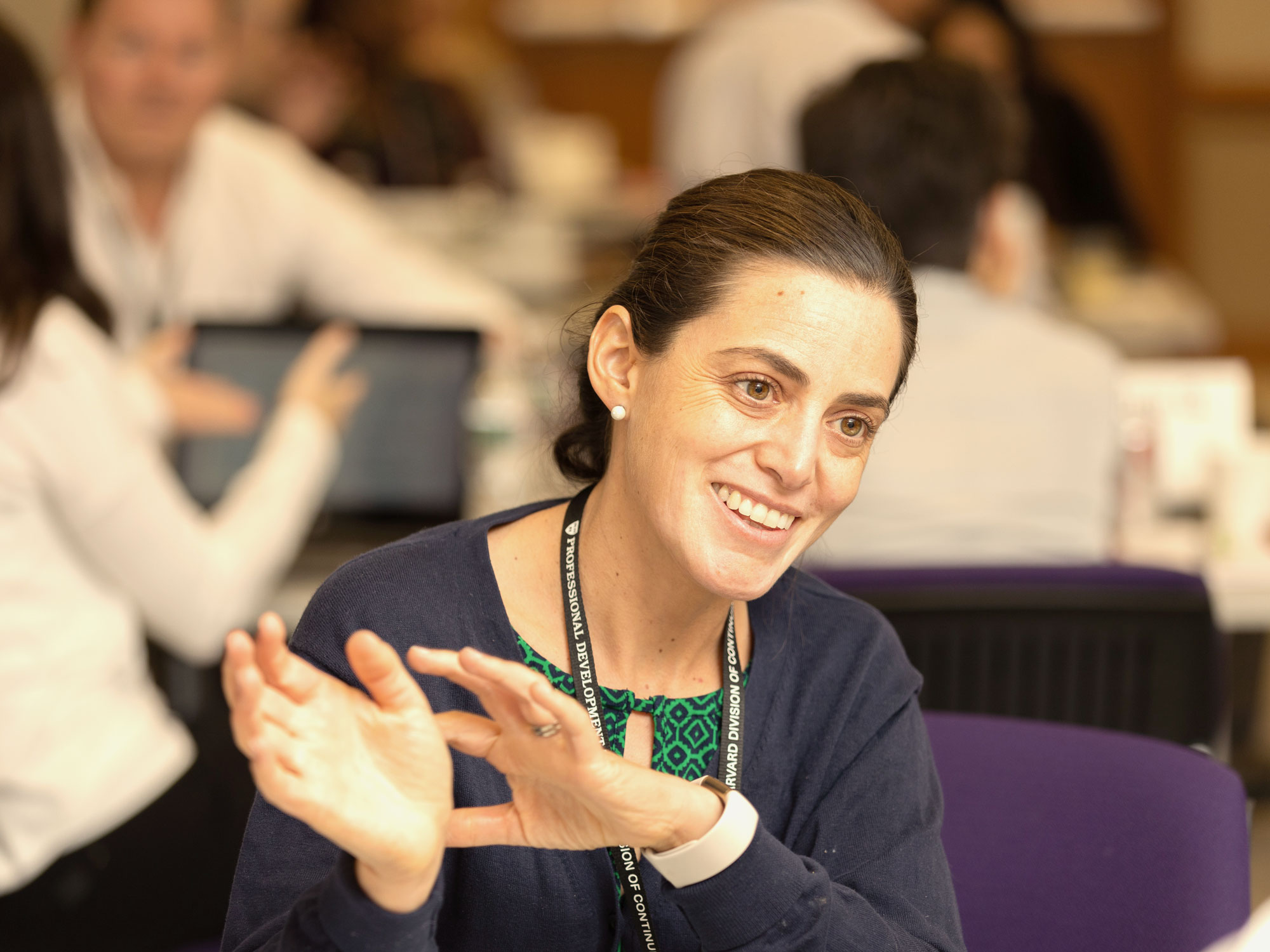 a brunette woman with a ponytail smiling and gesturing with her hands in a classroom