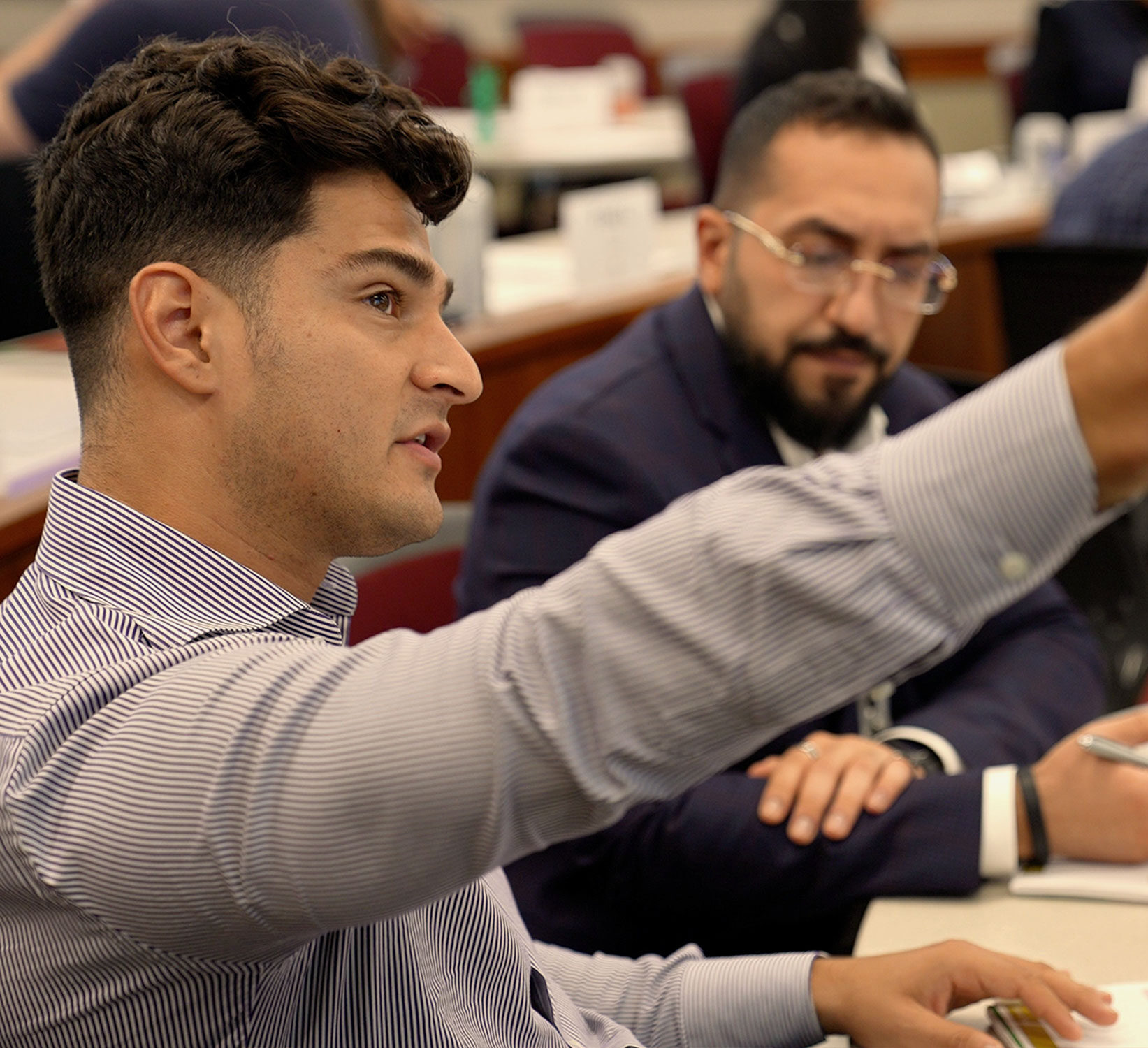 A young professional gestures at something off screen while talking at a professional development program.