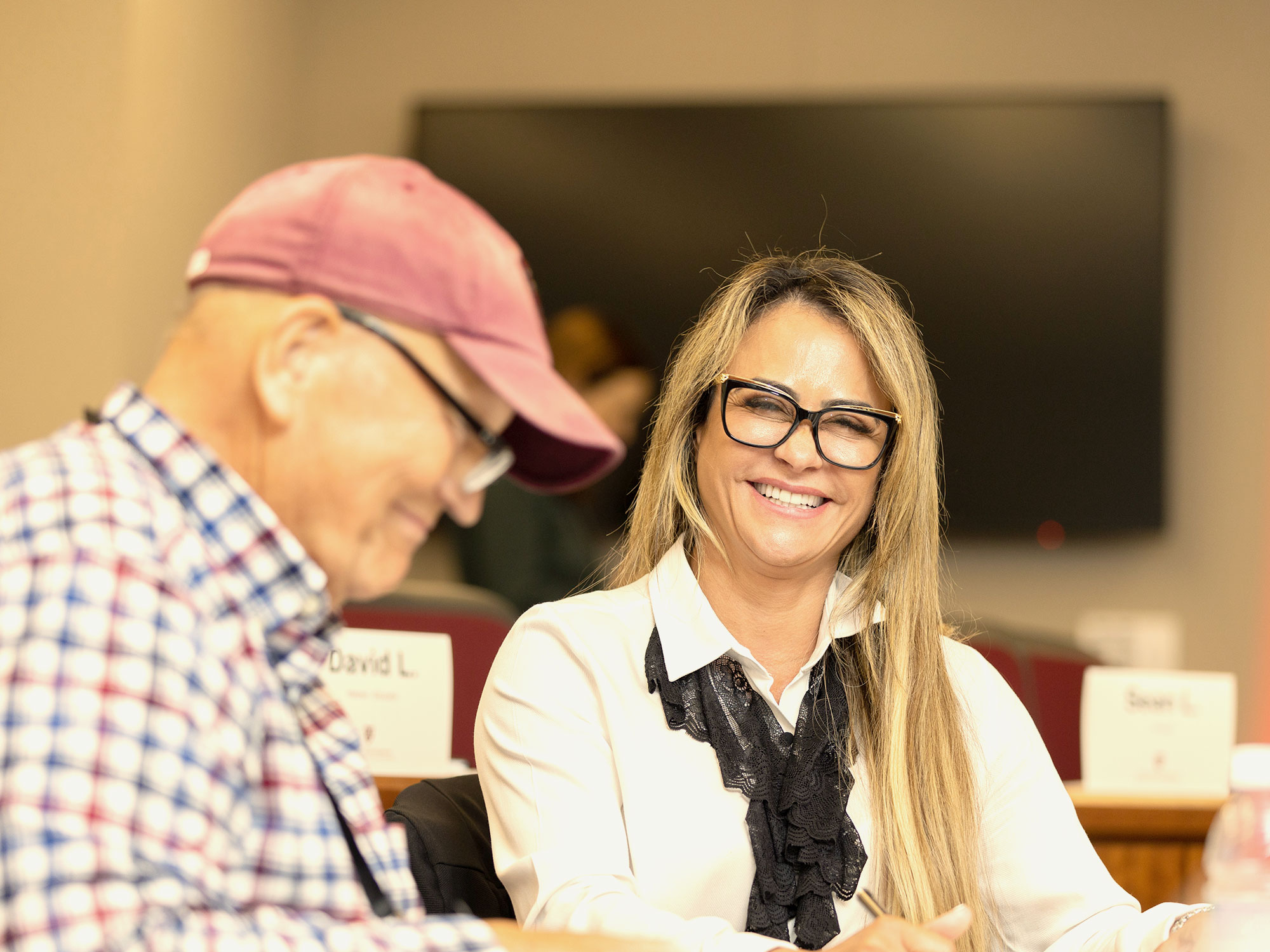 A woman in glasses smiles during a classroom activity.