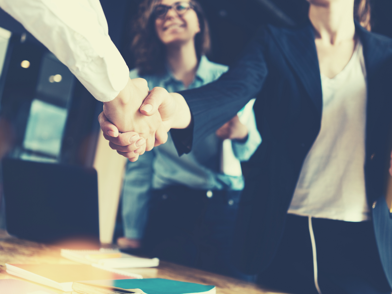 two people shake hands over conference table
